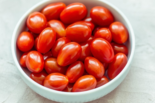 Tomates cherry rojos frescos en un tazón cerca de fondo gris