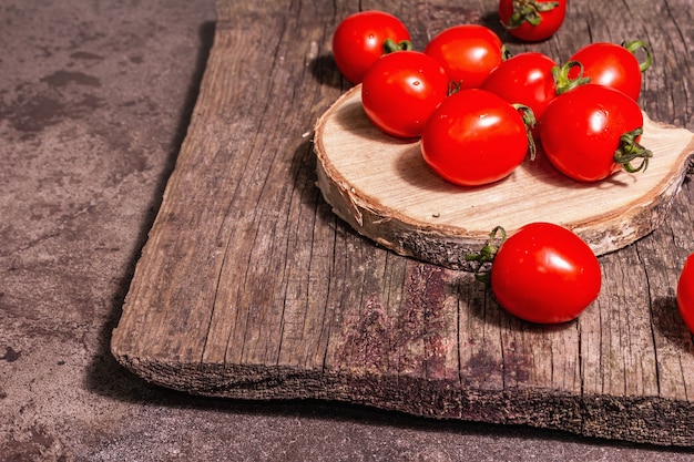 Tomates cherry rojos sobre un soporte de madera. Verduras dulces frescas, producto de agricultores orgánicos. Luz dura moderna, sombra oscura, tabla de cortar, fondo de piedra de mármol, espacio de copia