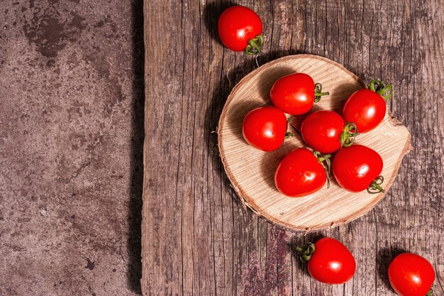 Tomates cherry rojos sobre un soporte de madera. Verduras dulces frescas, producto de agricultores orgánicos. Luz dura moderna, sombra oscura, tabla de cortar, fondo de piedra de mármol, vista superior