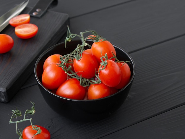 Tomates cherry sobre una tabla para cortar y una mesa de madera oscura.