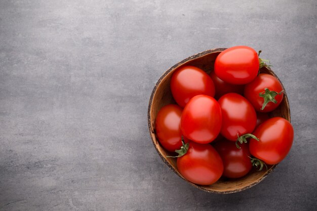 Tomates cherry. Tres tomates cherry en un cuenco de madera sobre un fondo gris.