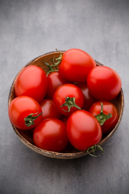 Tomates cherry. Tres tomates cherry en un cuenco de madera sobre una mesa gris.