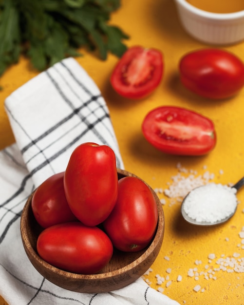 Tomates ciruela maduros en una placa de madera, sal en una cuchara y rúcula fresca