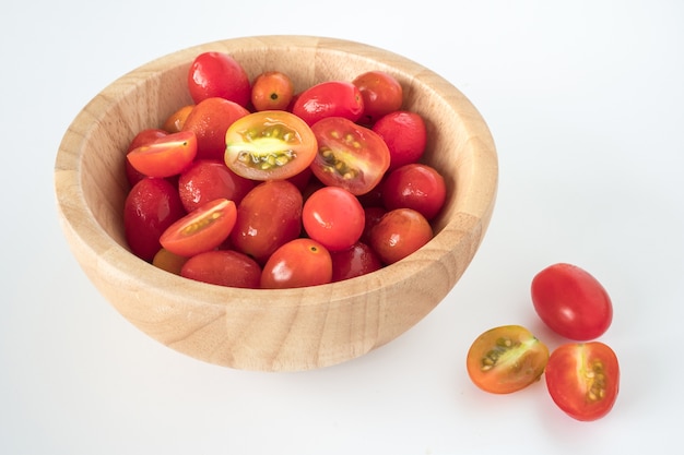 Tomates de ciruelo en cuenco de madera en el fondo blanco.