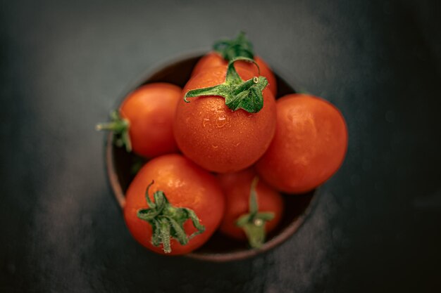 Tomates de cóctel rojos maduros en un recipiente sobre una mesa negra Verduras jugosas rojas y negras Productos rojos