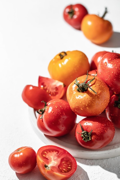 Tomates coloridos frescos laranja amarelo vermelho na chapa branca com sombras duras no plano de fundo texturizado