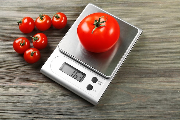 Tomates com balanças de cozinha digital em fundo de madeira