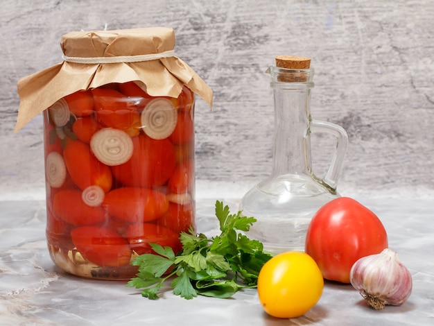 Tomates conservados en un frasco de vidrio, una botella de vinagre y tomates frescos, hojas de perejil, ajo en la mesa de la cocina.