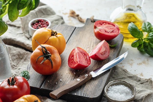 Tomates crudos en una tabla de cortar de madera rodeada de ingredientes Fondo de cocina rústica