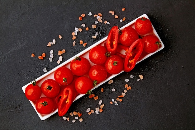 Tomates de cereja lavados frescos e fatias de páprica em um prato oblongo branco com sal rosa e gotas de água em um preto