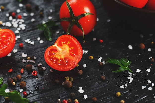 Tomates de cereja vermelhos suculentos com especiarias, sal grosso e verdes. tomates doces e maduros para saladas e como ingredientes para cozinhar