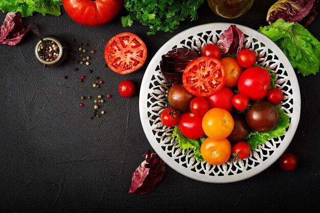 Tomates de cores diferentes com ervas verdes em uma bacia em um fundo preto.