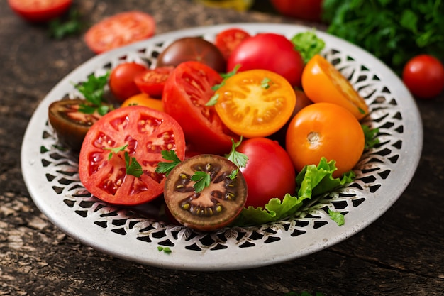 Tomates de cores diferentes com ervas verdes em uma bacia em um fundo preto.