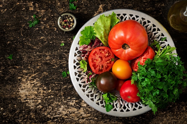 Tomates de cores diferentes com ervas verdes em uma bacia em um fundo preto.