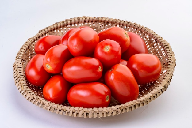 Tomates dentro de la cesta de paja aislado sobre fondo blanco.