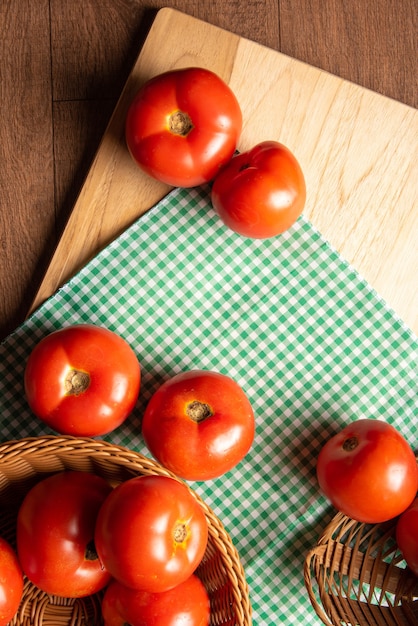 Foto tomates dispuestos en una canasta y sobre una tabla para cortar madera