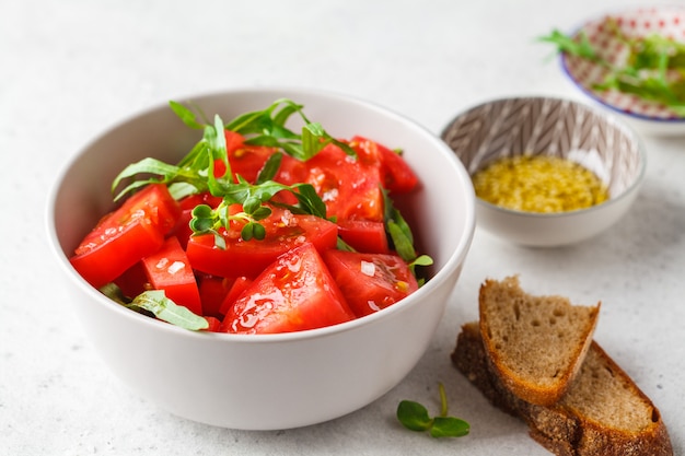 Tomates e salada da rúcula com brotos e azeite na bacia cinzenta.