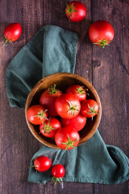 Tomates enteros crudos maduros en un recipiente sobre una mesa de madera Cosechar productos locales Vista superior y vertical