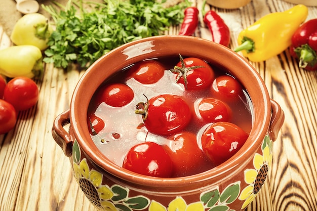 Tomates en escabeche enlatados caseros con eneldo y hierbas de ajo en un tazón sobre una mesa de madera