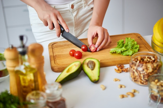 Tomates felizes novos do corte da mulher para fazer a salada na cozinha bonita com ingredientes frescos verdes dentro. comida saudável e conceito de dieta. perder peso