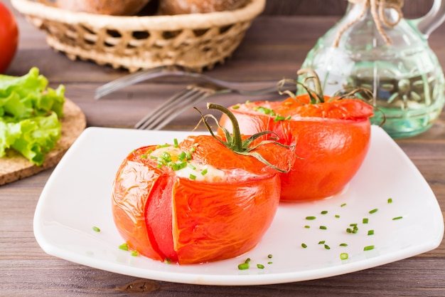 Tomates frescos al horno con queso y huevo espolvoreado con cebolla verde en un plato sobre una mesa de madera