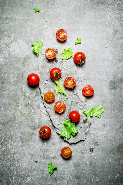 Tomates frescos com alface em um carrinho de pedra. Sobre um fundo de pedra.