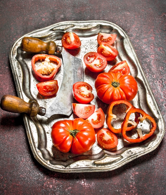 Tomates frescos con un cuchillo viejo en una bandeja de acero sobre un fondo rústico
