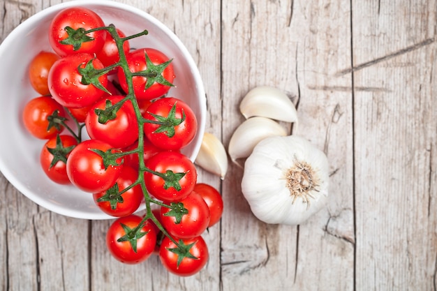 Tomates frescos en el cuenco blanco y el ajo crudo en la tabla de madera rústica.