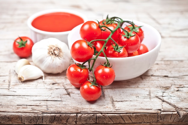 Tomates frescos en el cuenco blanco, la salsa y el ajo crudo en la tabla de madera rústica.