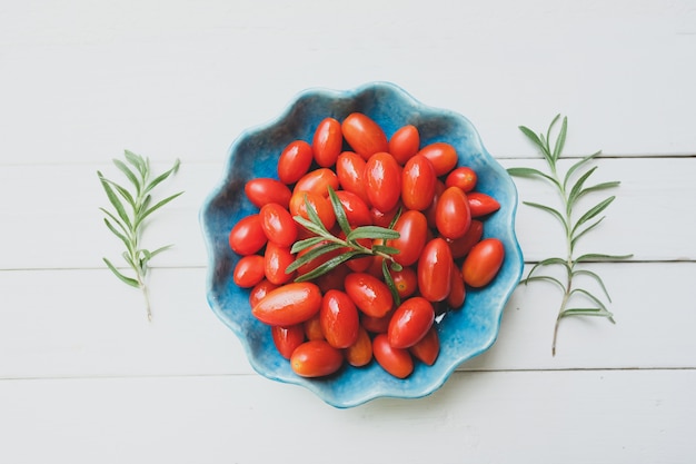 Tomates frescos en un cuenco y un romero azules en blanco