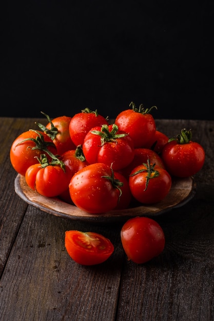 tomates frescos em um prato em um fundo escuro colhendo tomates