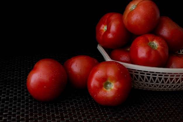 Tomates frescos em uma placa em um fundo escuro. uma cesta cheia de tomates