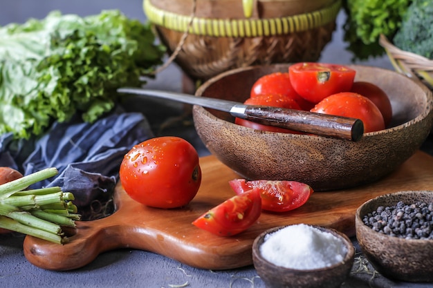 tomates frescos em uma tigela, em torno de legumes, cenoura, pimenta preta, milho, brócolis. Corte os tomates. Colheita de tomates.
