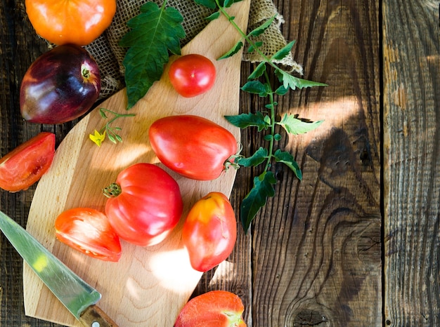 Tomates frescos de granja en una tabla de cortar en una mesa antigua de madera