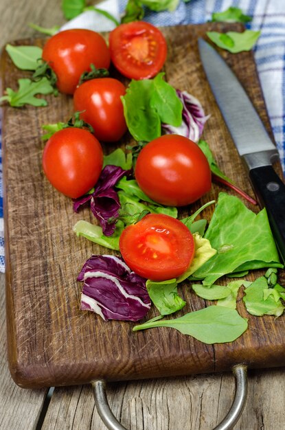 Tomates frescos y hojas de ensalada en tabla de cortar.