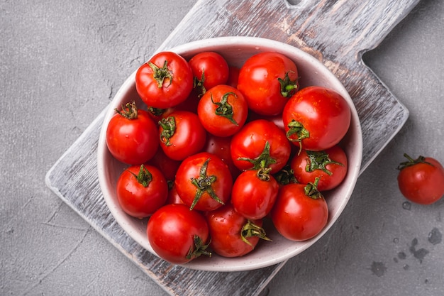 Tomates frescos maduros com gotas de água em uma tigela na velha tábua de madeira