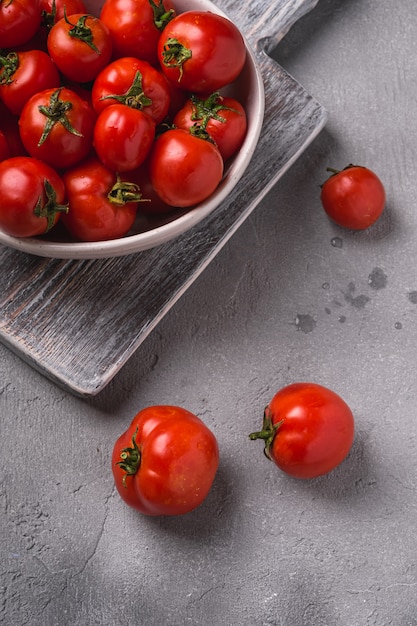 Tomates frescos maduros com gotas de água em uma tigela na velha tábua de madeira