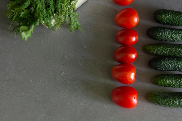 Tomates frescos pepinos verdes y ensalada de verduras aromáticas en una cesta de bambú colocada exactamente en una fila en la mesa de la cocina