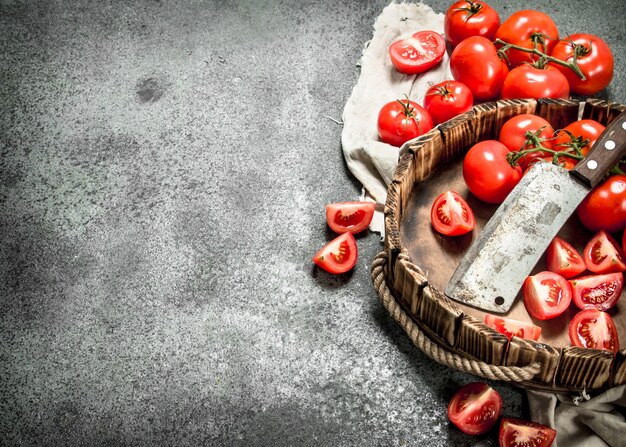 Tomates frescos en rodajas en la bandeja con un cuchillo viejo sobre fondo rústico