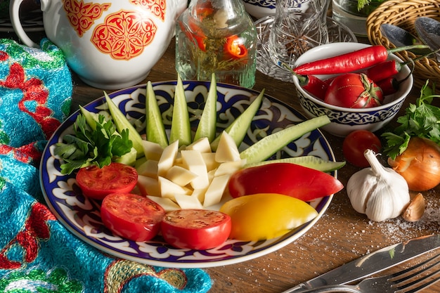 Tomates frescos sortidos, pimentões doces, pepinos, queijo e coentros em um prato com um padrão tradicional do Uzbeque