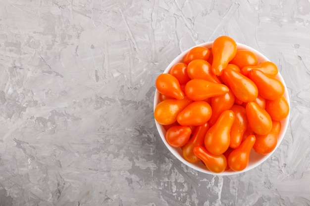 Tomates frescos de uva naranja en tazón de cerámica blanca sobre fondo de hormigón gris. vista superior.