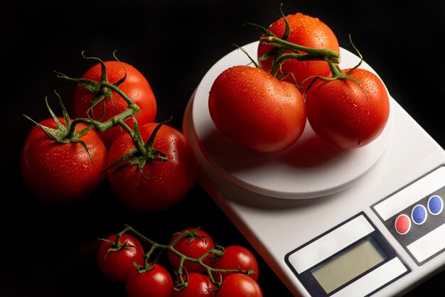 Tomates, hermosos tomates colocados en una escala de precisión sobre fondo negro, enfoque selectivo.