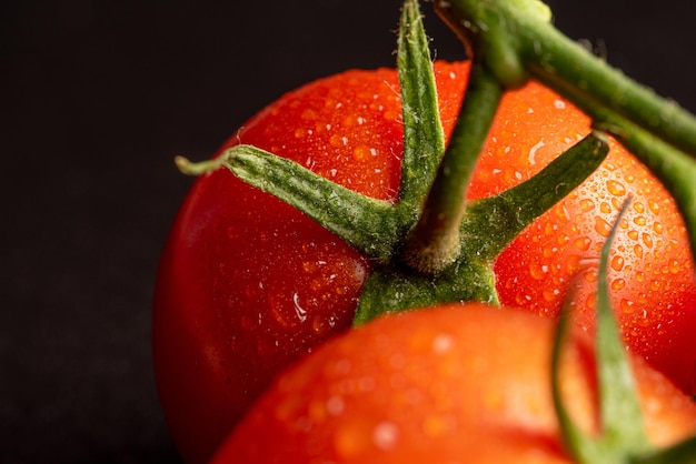 Tomates, lindos tomates com gotas de água dispostas em uma superfície escura, foco seletivo.