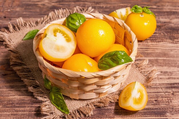 Tomates maduros amarelos com manjericão fresco. Novos vegetais de colheita em uma cesta de vime. Mesa de madeira vintage, cópia espaço