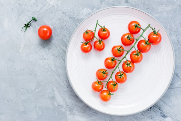 Tomates maduros cereja maduros em um galho em um prato em concreto