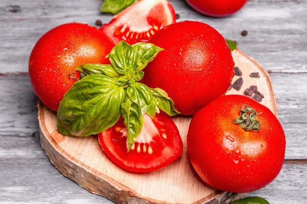 Tomates maduros com folhas frescas de manjericão, sal preto e pimenta do reino. Vegetais inteiros e cortados pela metade, fundo de tábuas de madeira velhas, close-up