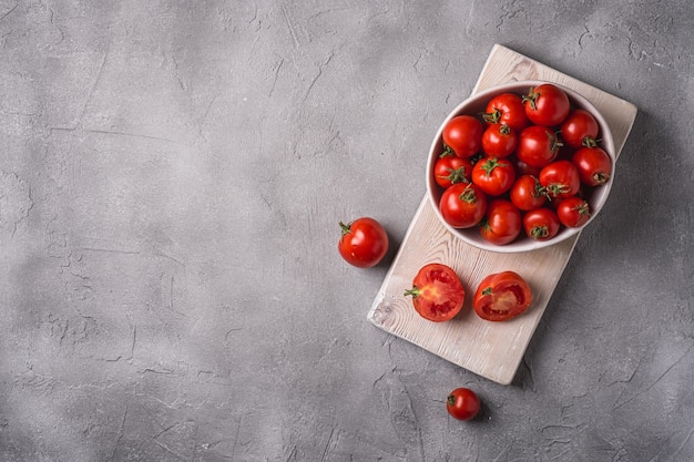 Tomates maduros frescos enteros y en rodajas en un tazón y sobre una tabla de cortar de madera vieja, espacio de copia de hormigón de piedra