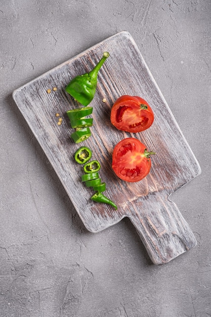 Tomates maduros frescos en rodajas con pimientos picantes en la tabla de cortar de madera vieja, hormigón de piedra