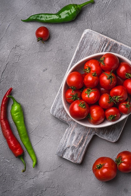 Tomates maduros frescos en un tazón sobre la vieja tabla de cortar de madera con pimientos picantes, hormigón de piedra