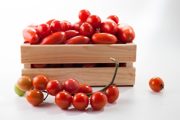 Tomates maduros en mentira en una caja de madera sobre un fondo blanco.